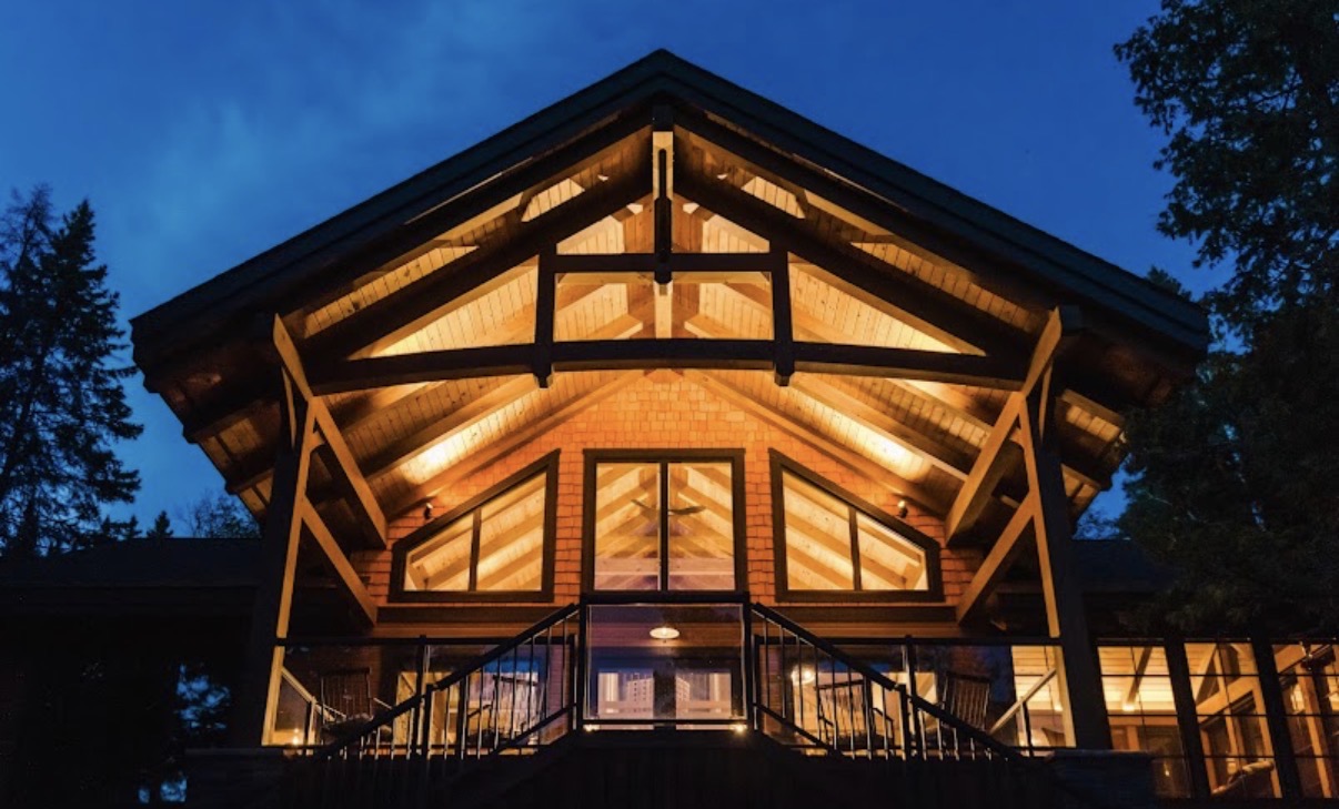 Timber-frame lodge glowing at dusk built by Timber Wolf Construction